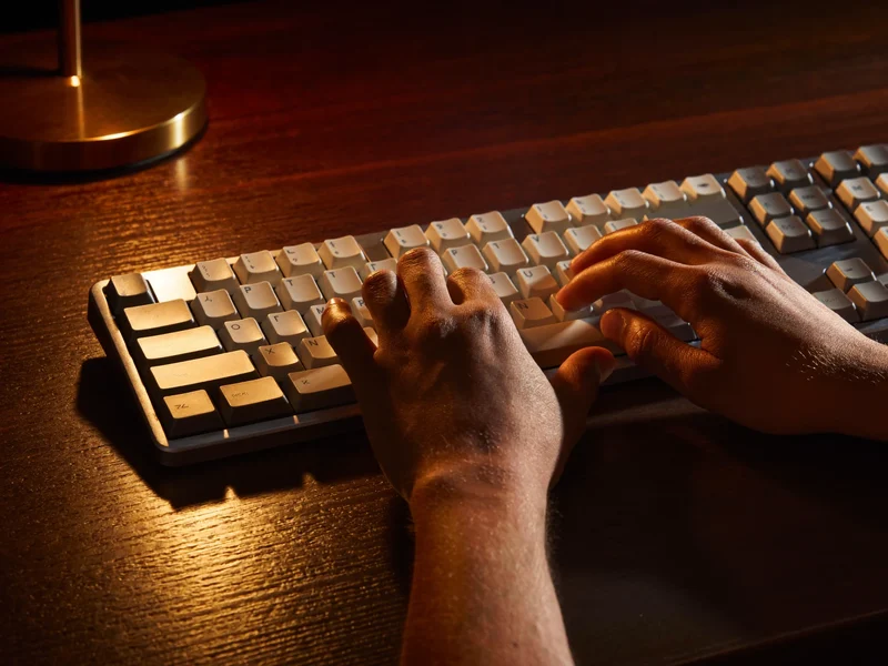 Detailansicht der Hände beim Tippen auf einer Tastatur im Lampenlicht
